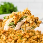Side angle closeup of a spoonful of Chicken and Stuffing Casserole hovering over a white casserole dish.
