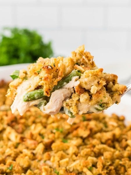 Side angle closeup of a spoonful of Chicken and Stuffing Casserole hovering over a white casserole dish.