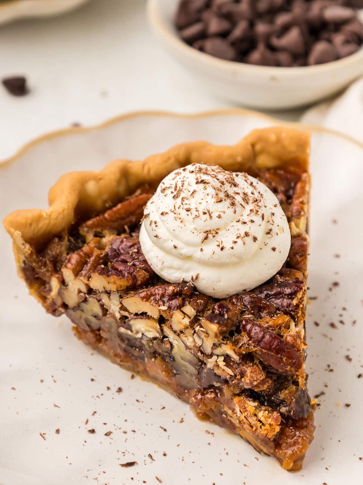 S slice of Chocolate Pecan Pie with whipped cream on served on a white plate.