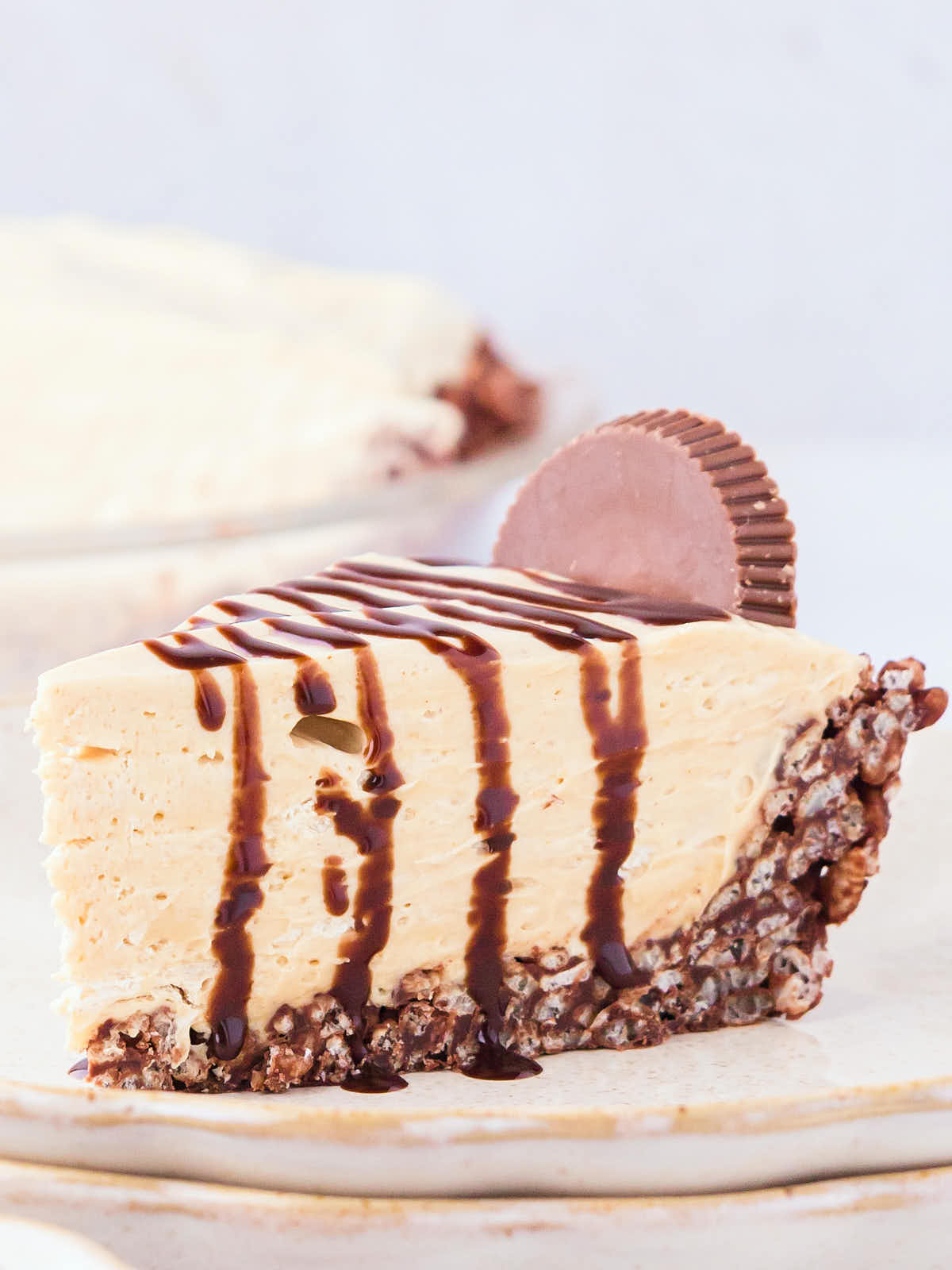 A slice of No-Bake Peanut Butter Pie drizzled with chocolate syrup on top served on a white plate.