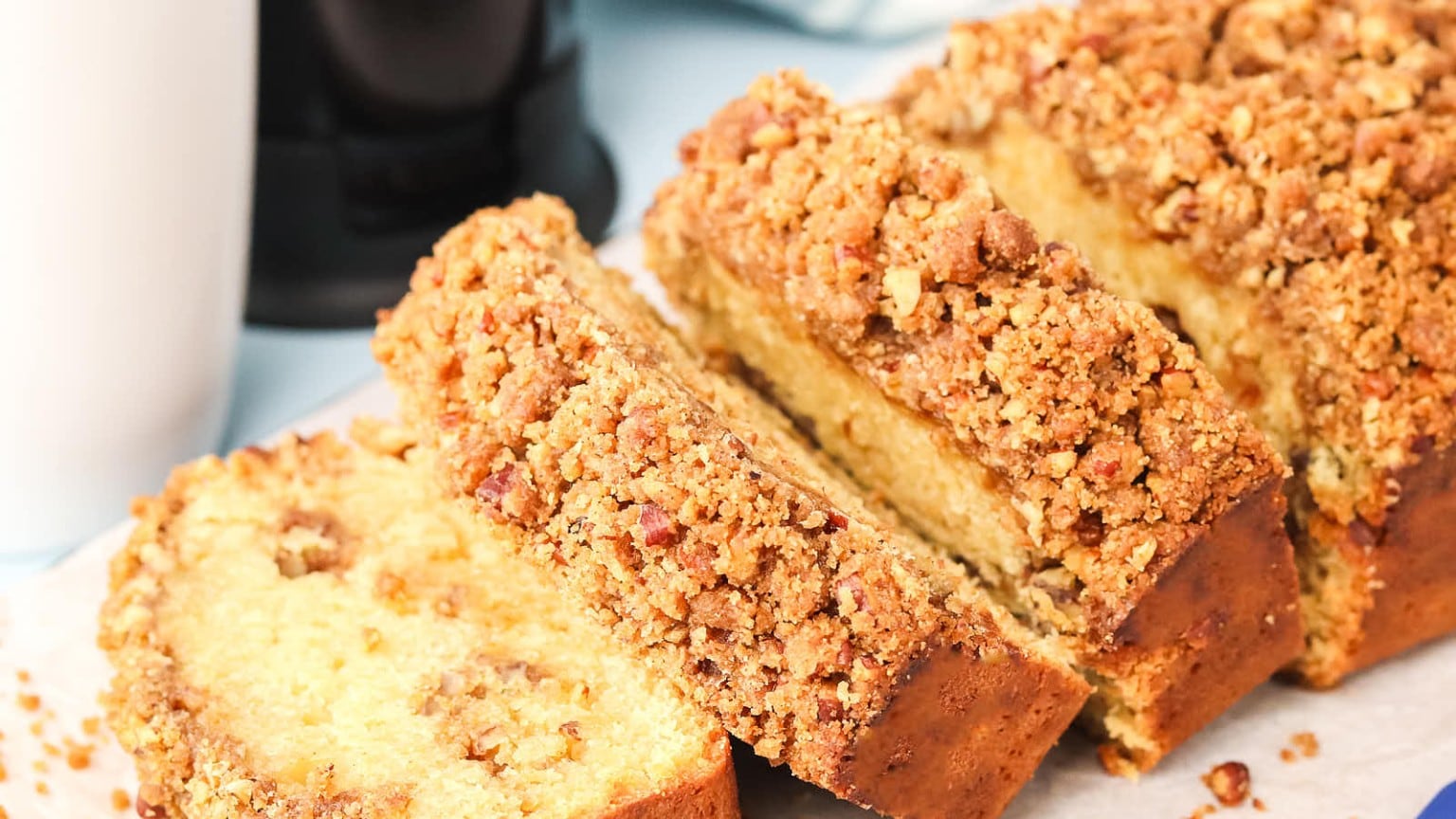 A delicious loaf of buttery cake topped with a crumbly nut streusel, sliced and ready to serve on a light blue surface.