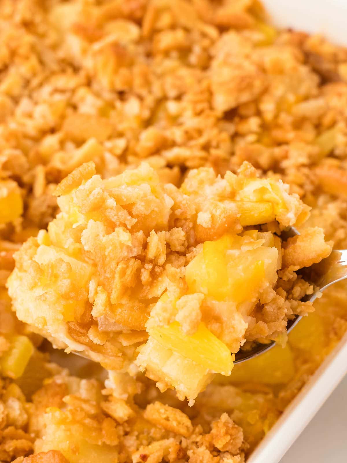 Removing a scoop of Pineapple Casserole with a serving spoon out of a white baking dish.