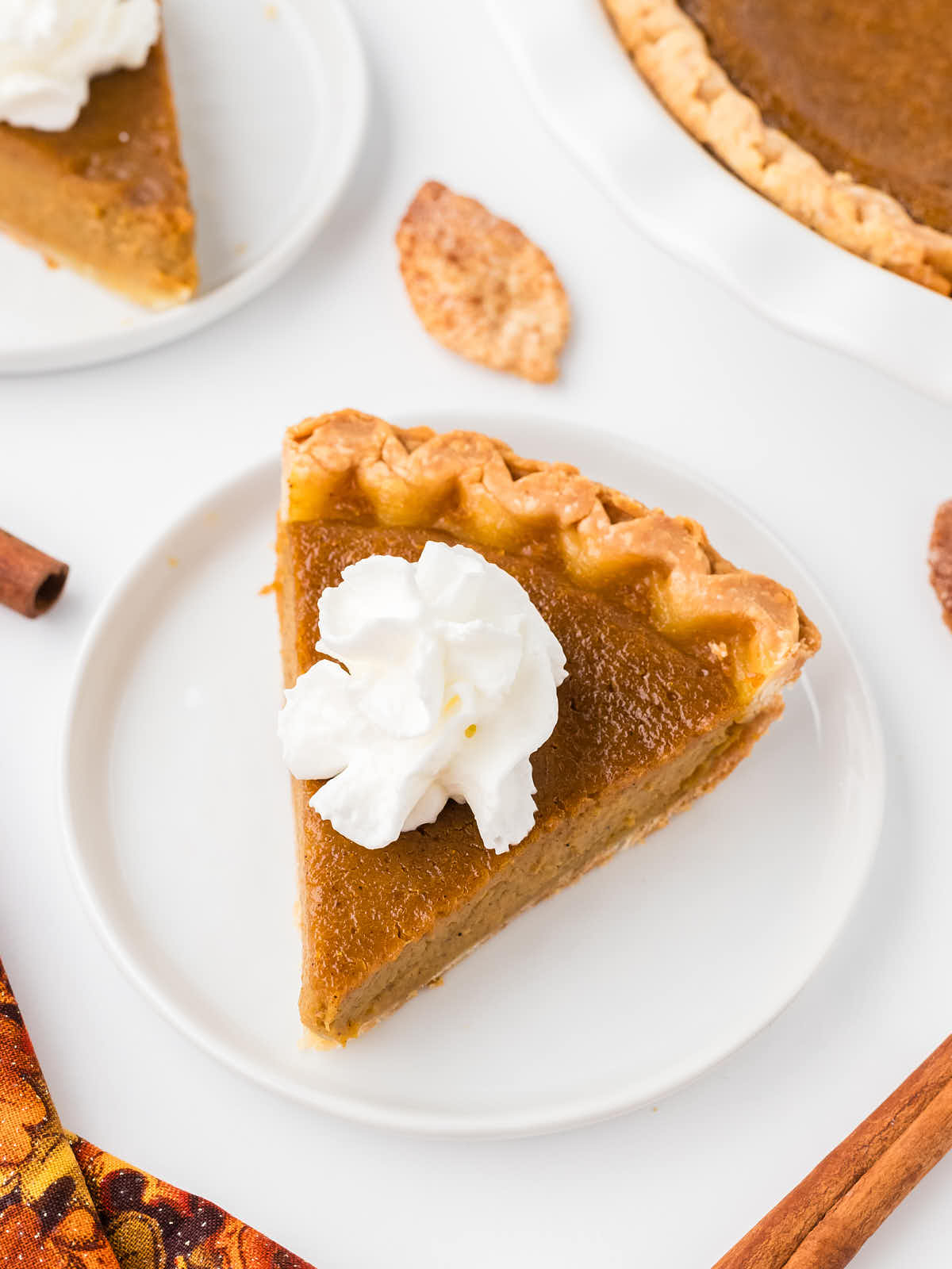 Topdown view of a slice of Pumpkin Pie with whipped cream served on a white plate.