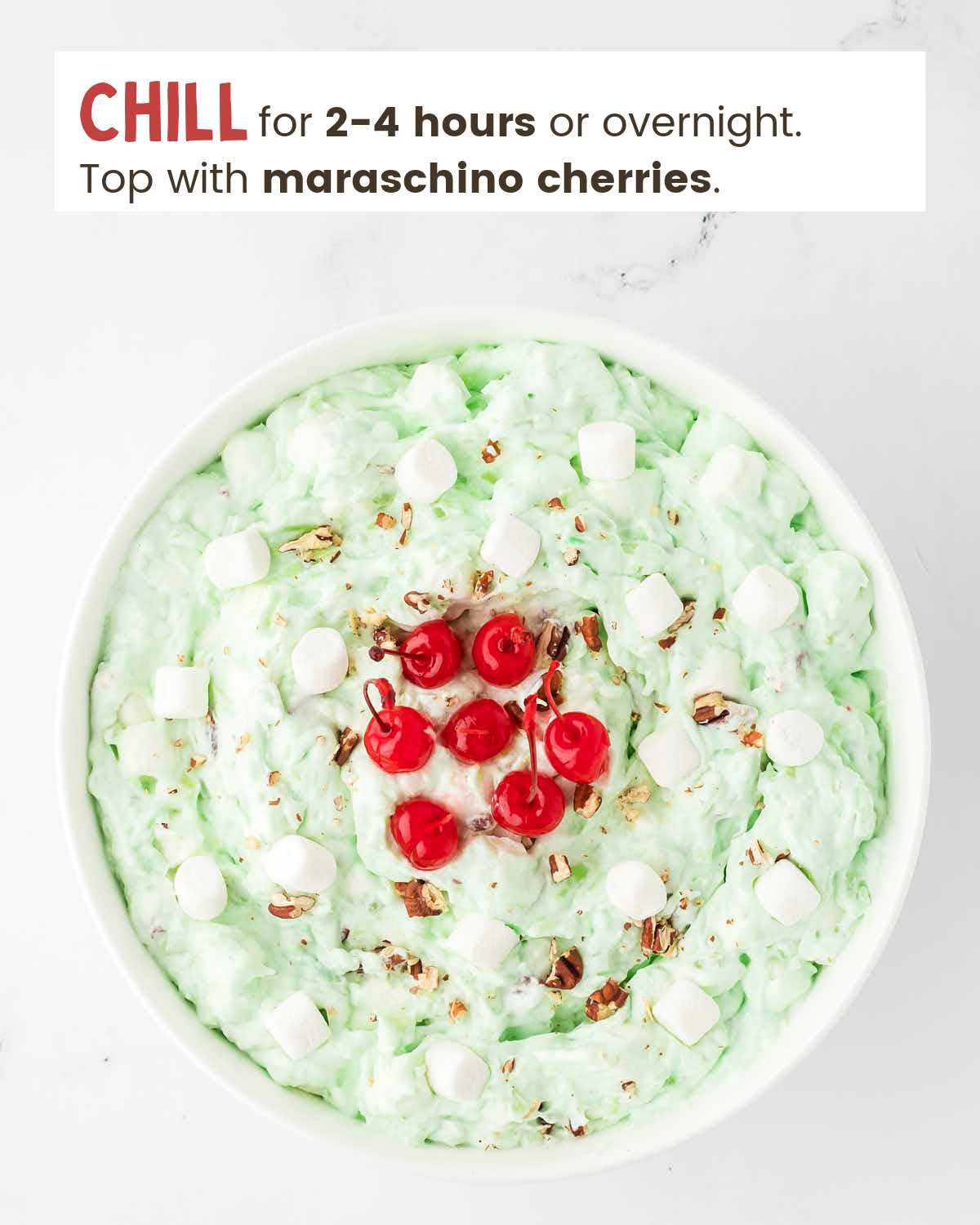 Watergate salad topped with chopped pecans and maraschino cherries in a bowl.