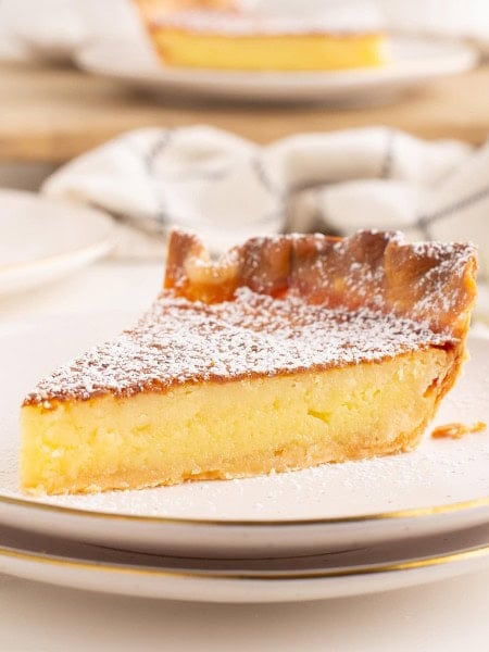 A slice of Chess Pie on a white plate drizzled with powdered sugar.
