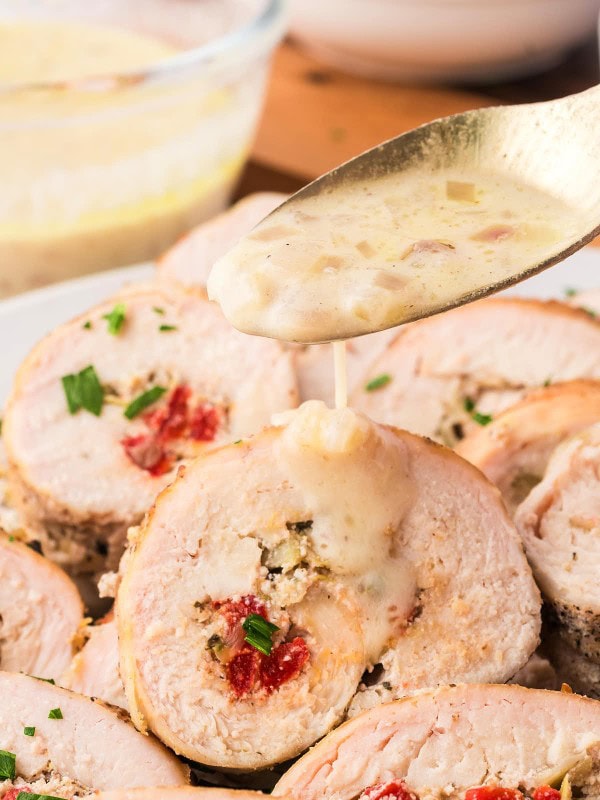 Drizzling white wine shallot sauce over sliced Chicken Rouladen.