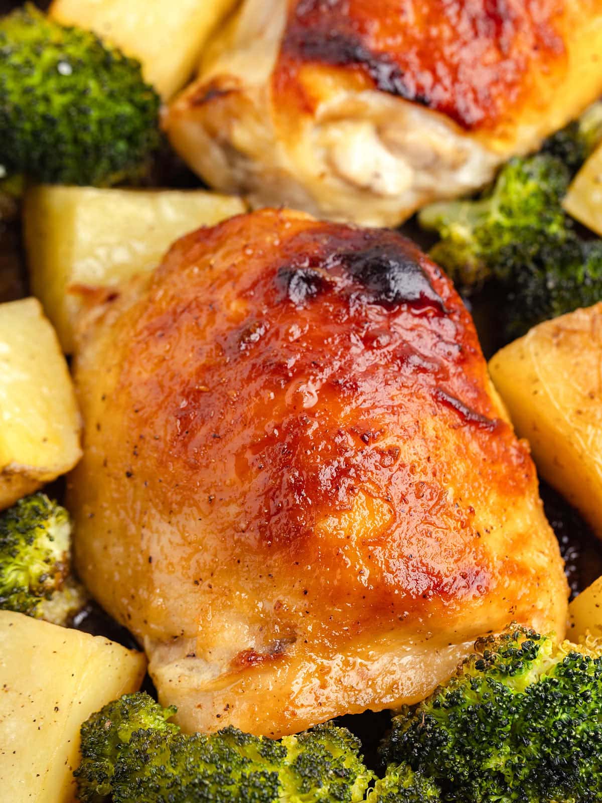 Closeup of a chicken thigh on a sheet pan with potatoes and broccoli.
