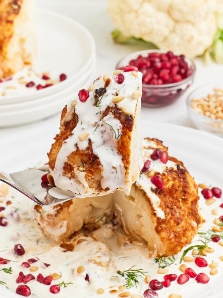 Lifting a slice of a Whole Roasted Cauliflower drizzled with Cream Sauce.