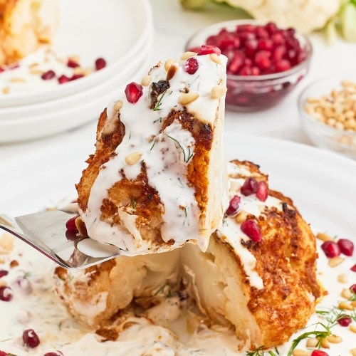 Lifting a slice of a Whole Roasted Cauliflower drizzled with Cream Sauce.