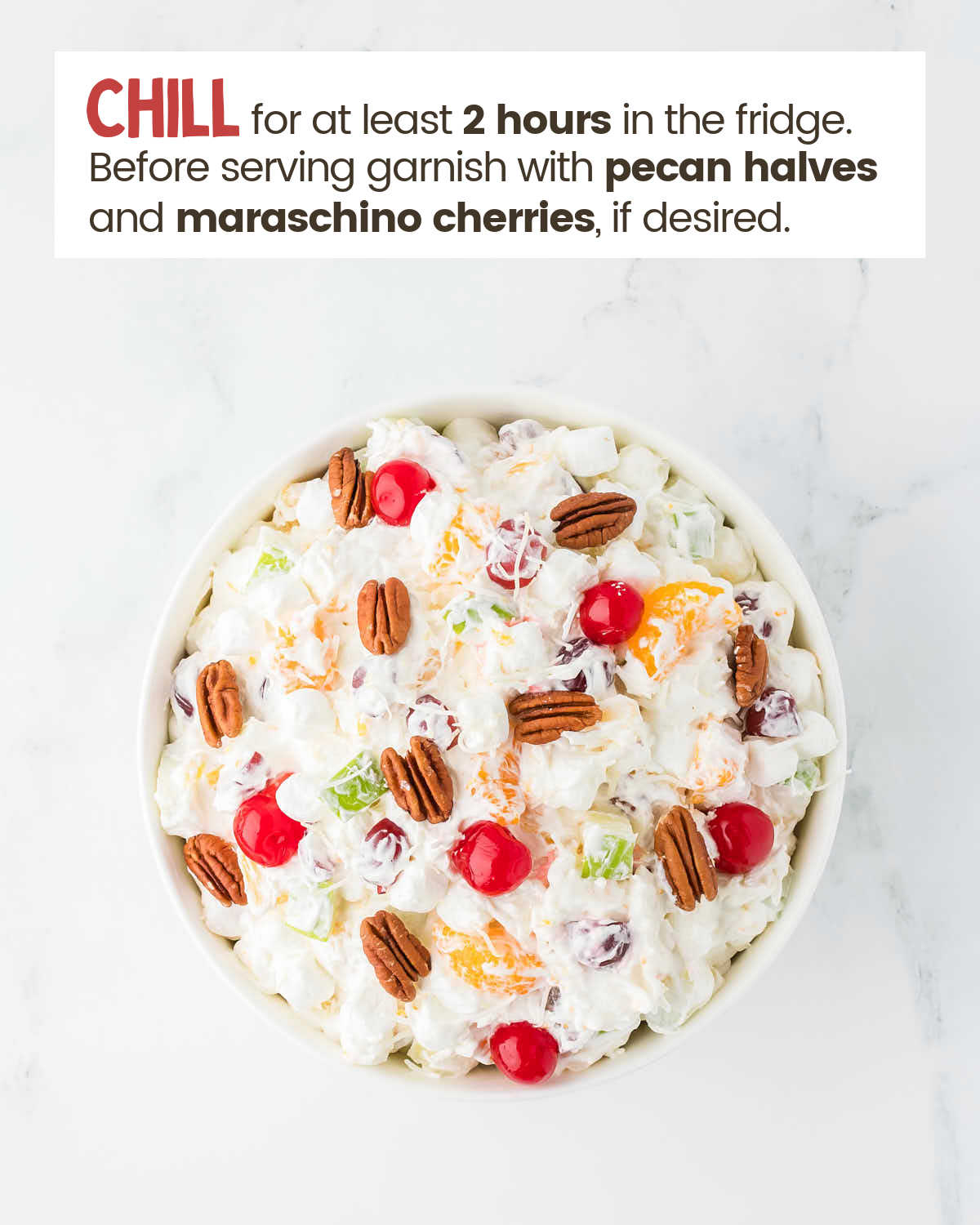 Ambrosia Salad in a bowl topped with pecan halves and maraschino cherries.