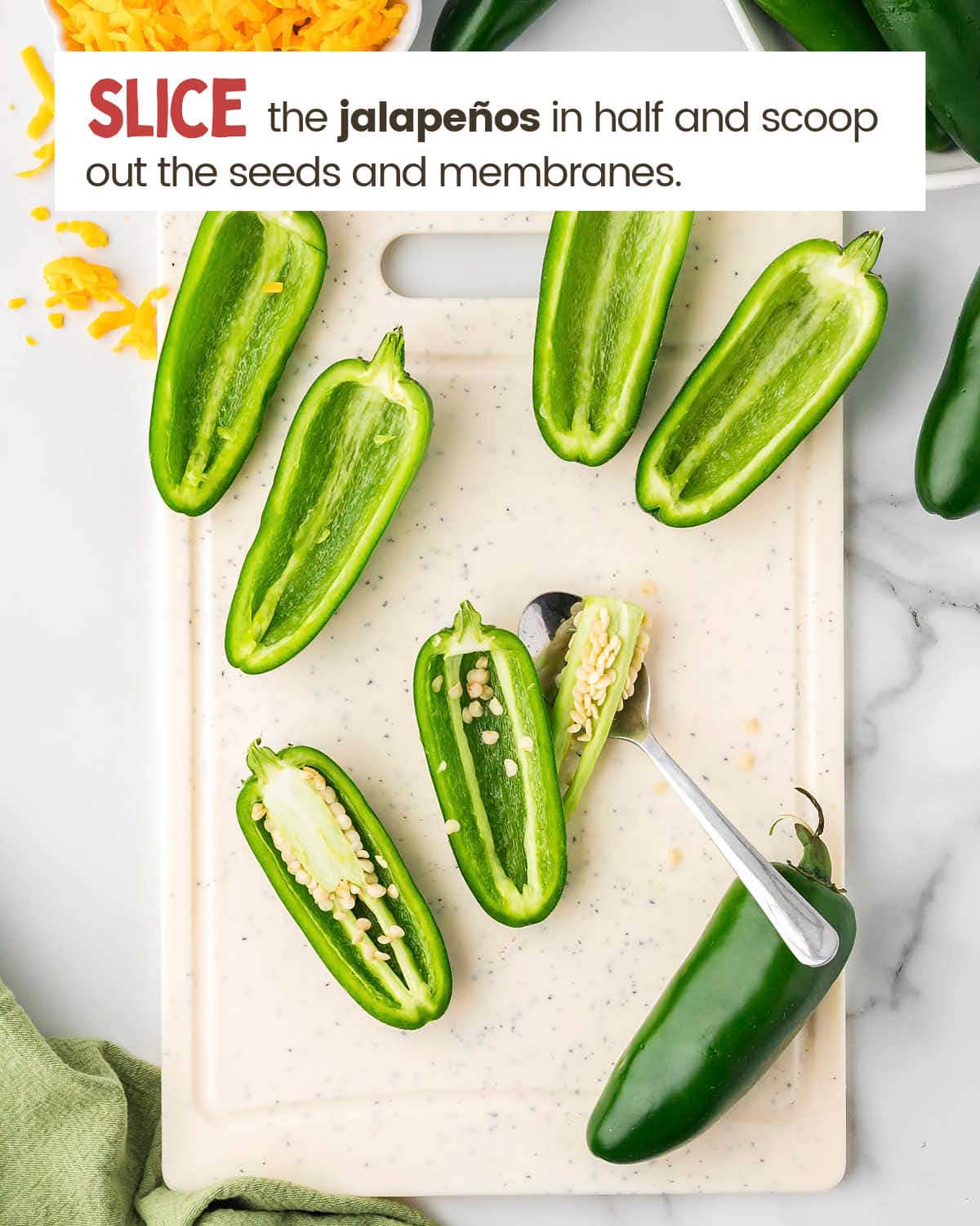 Sliced jalapeños on a cutting board with a spoon used to scoop out the seeds.