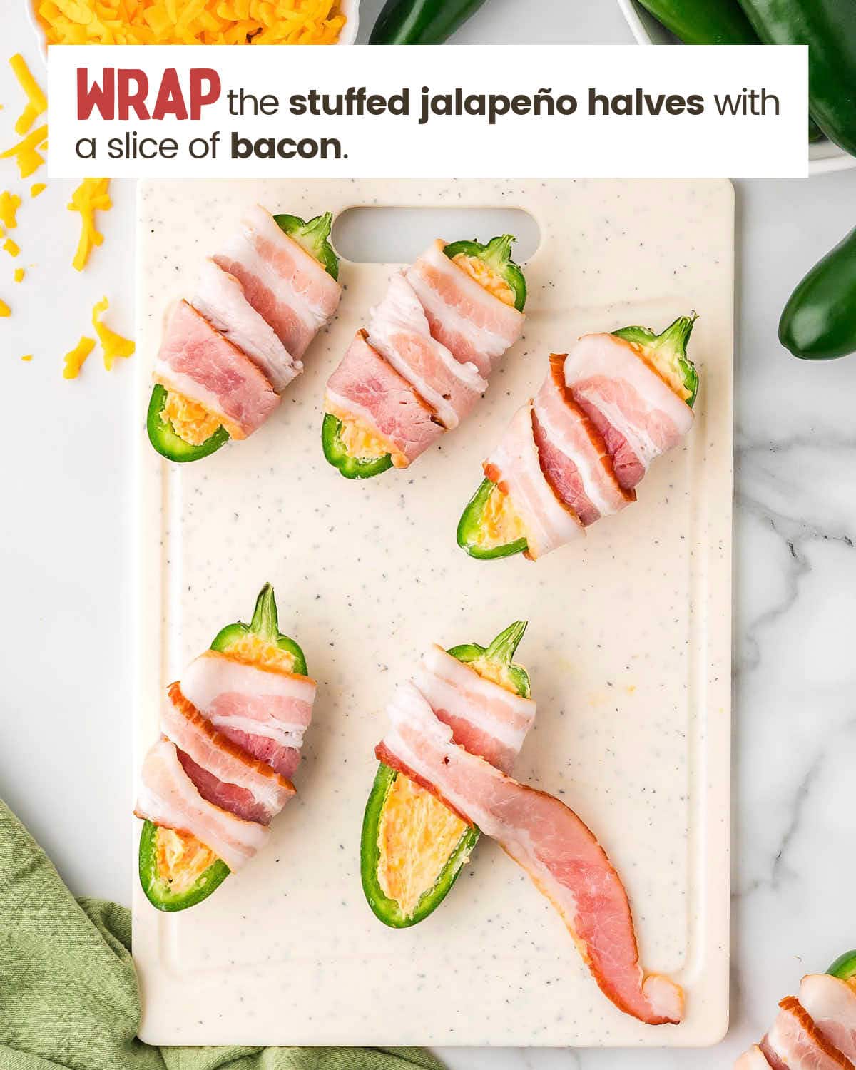 Jalapeños stuffed with a cheese mixture wrapped with sliced bacon on a cutting board.