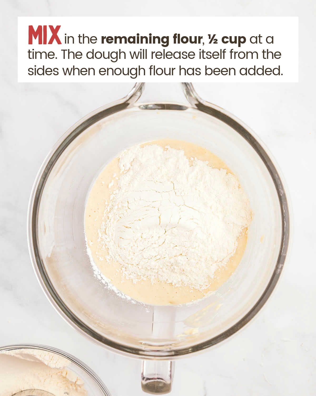 Flour covers a dough mixture in a glass bowl.