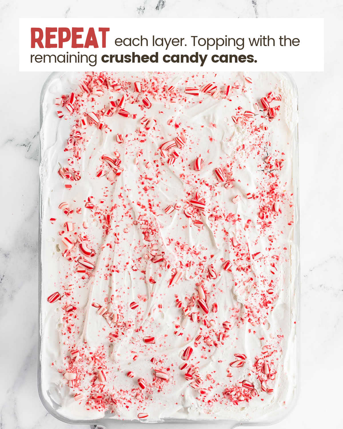 Cool whip layer of a Christmas Icebox cake sprinkled with crushed candy canes in a baking dish.