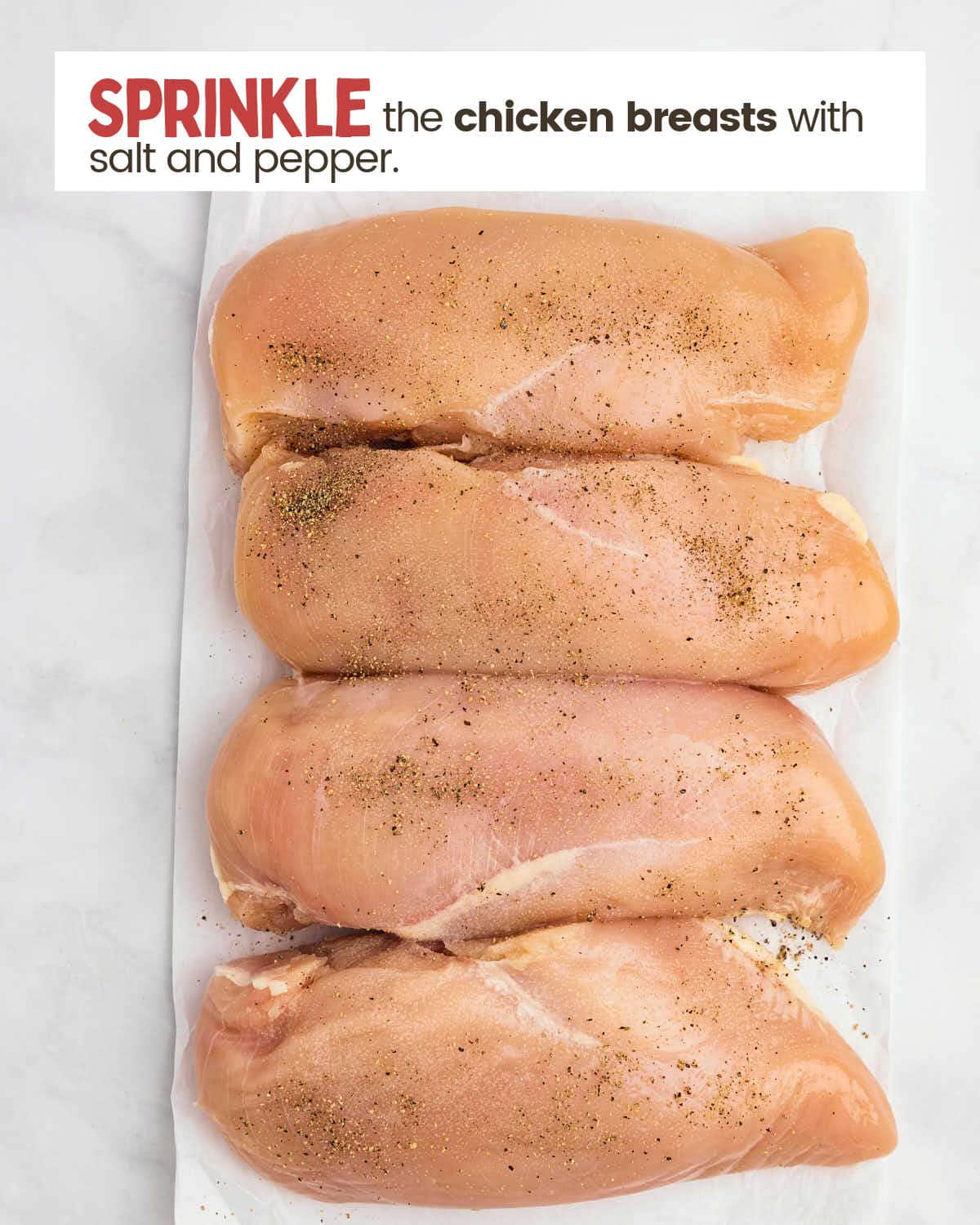 Four chicken breasts sprinkled with salt and pepper on a piece of parchment paper. 