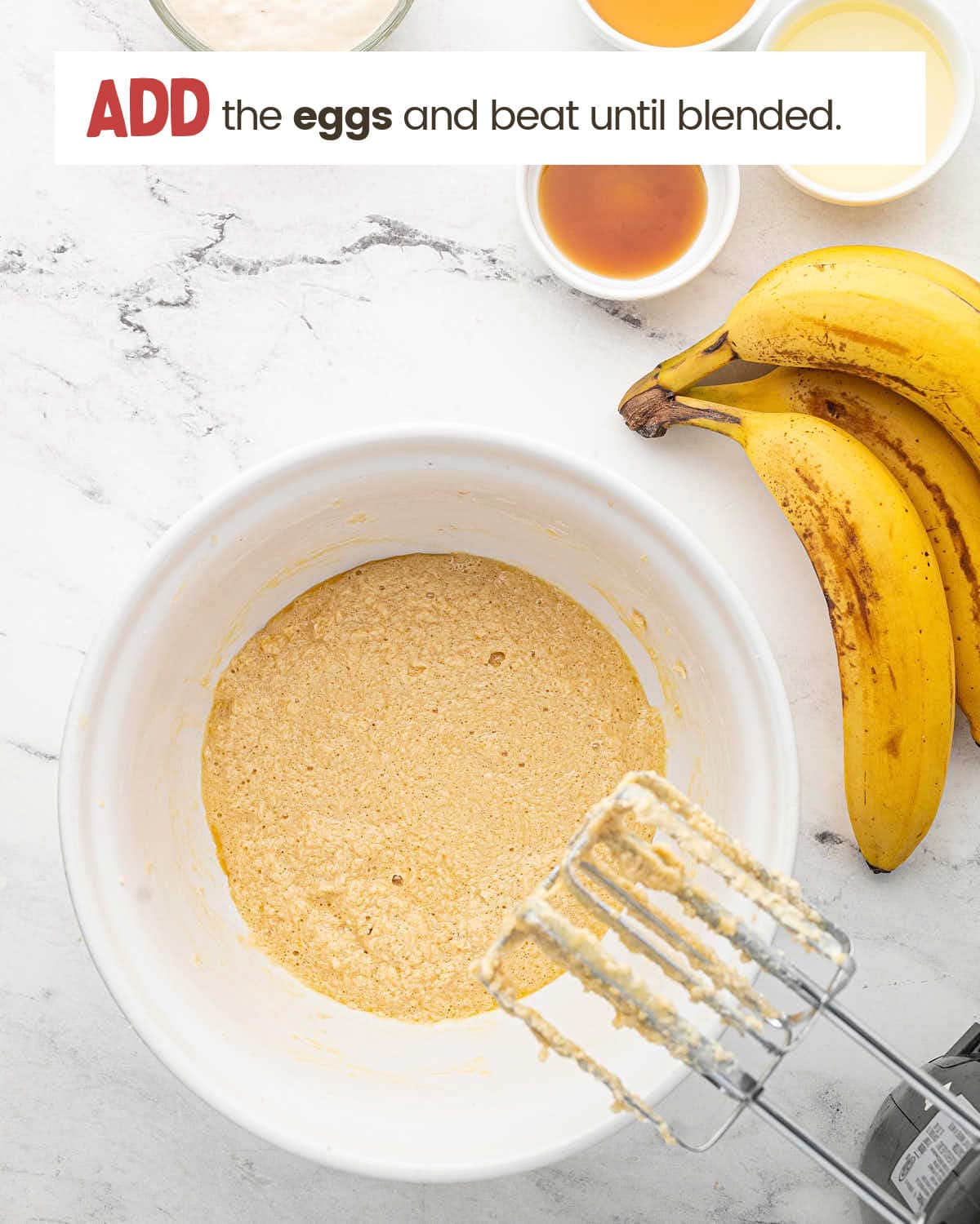 Bananas next to a bowl with a beaten mixture with beaters on edge of the bowl.