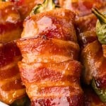 Closeup of a pile of Bacon Wrapped Jalapeño Poppers on a white plate.