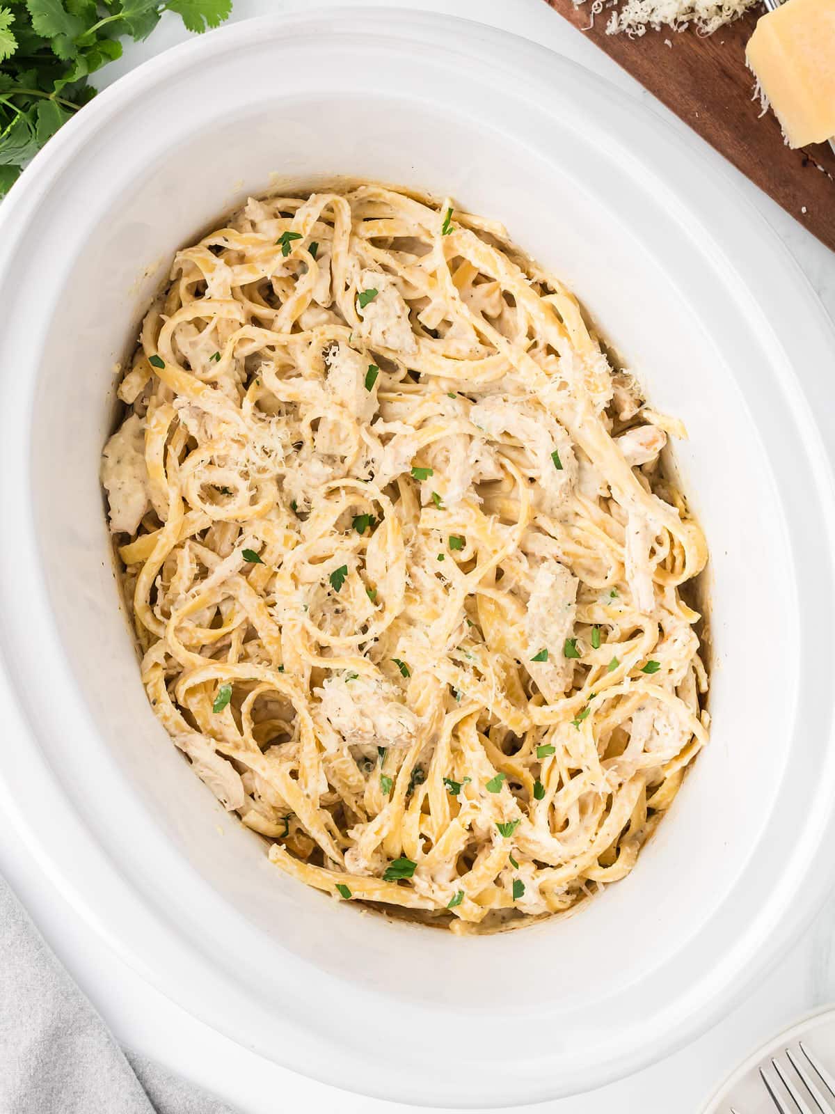 Top-down view of a white Crockpot with freshly cooked creamy Chicken Alfredo.