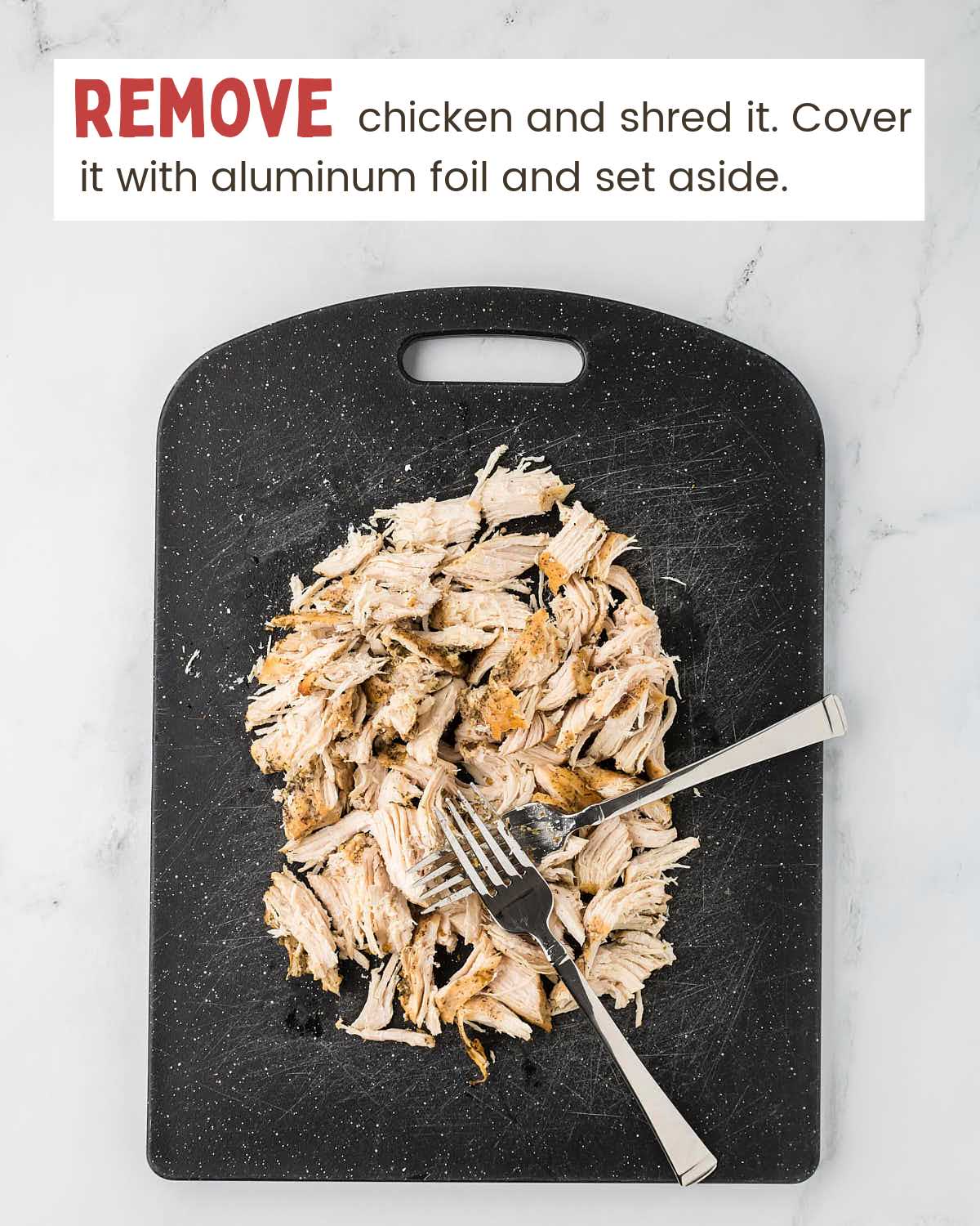 Shredded chicken on a black cutting board with two forks.