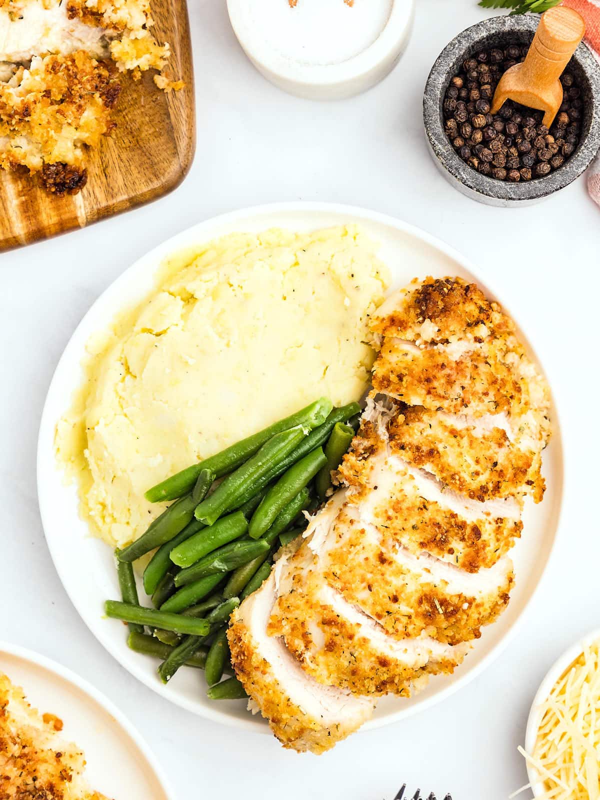 A plate filled with sliced Parmesan Crusted Chicken, mashed potatoes, and green beans.