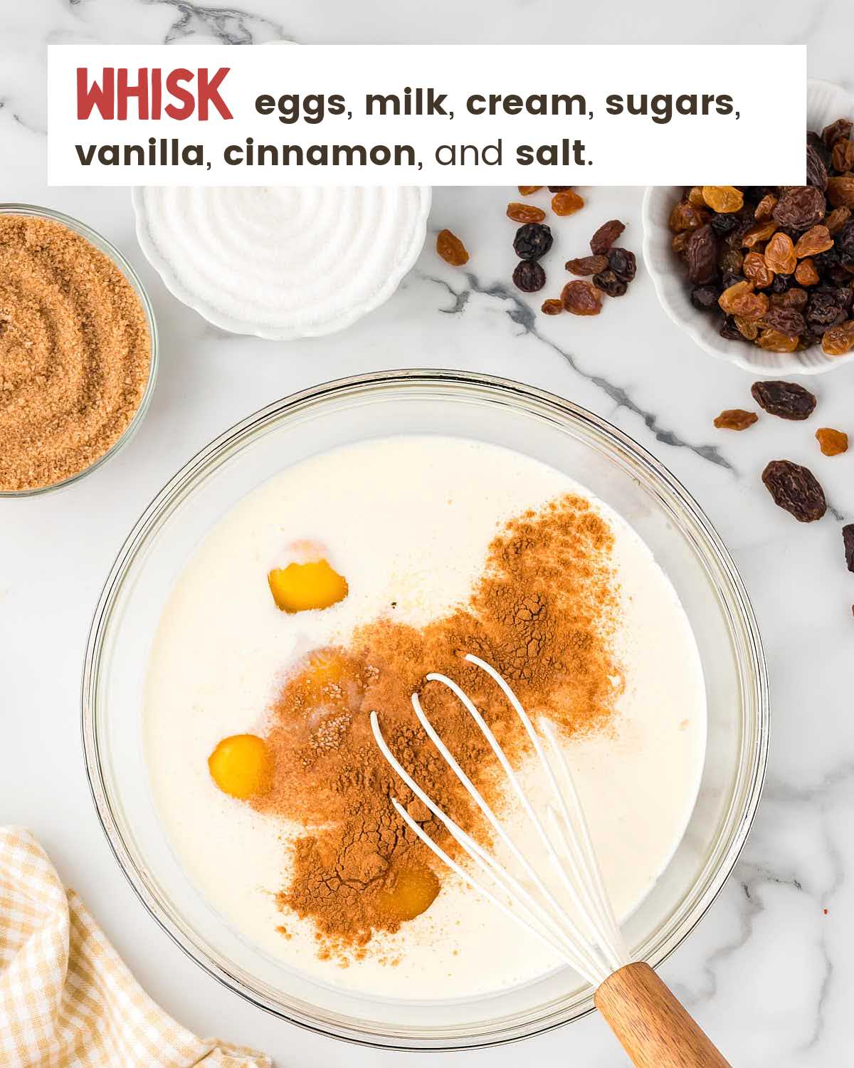 A whisk in a bowl with eggs, milk, cream, sugars, vanilla, and cinnamon, and salt.