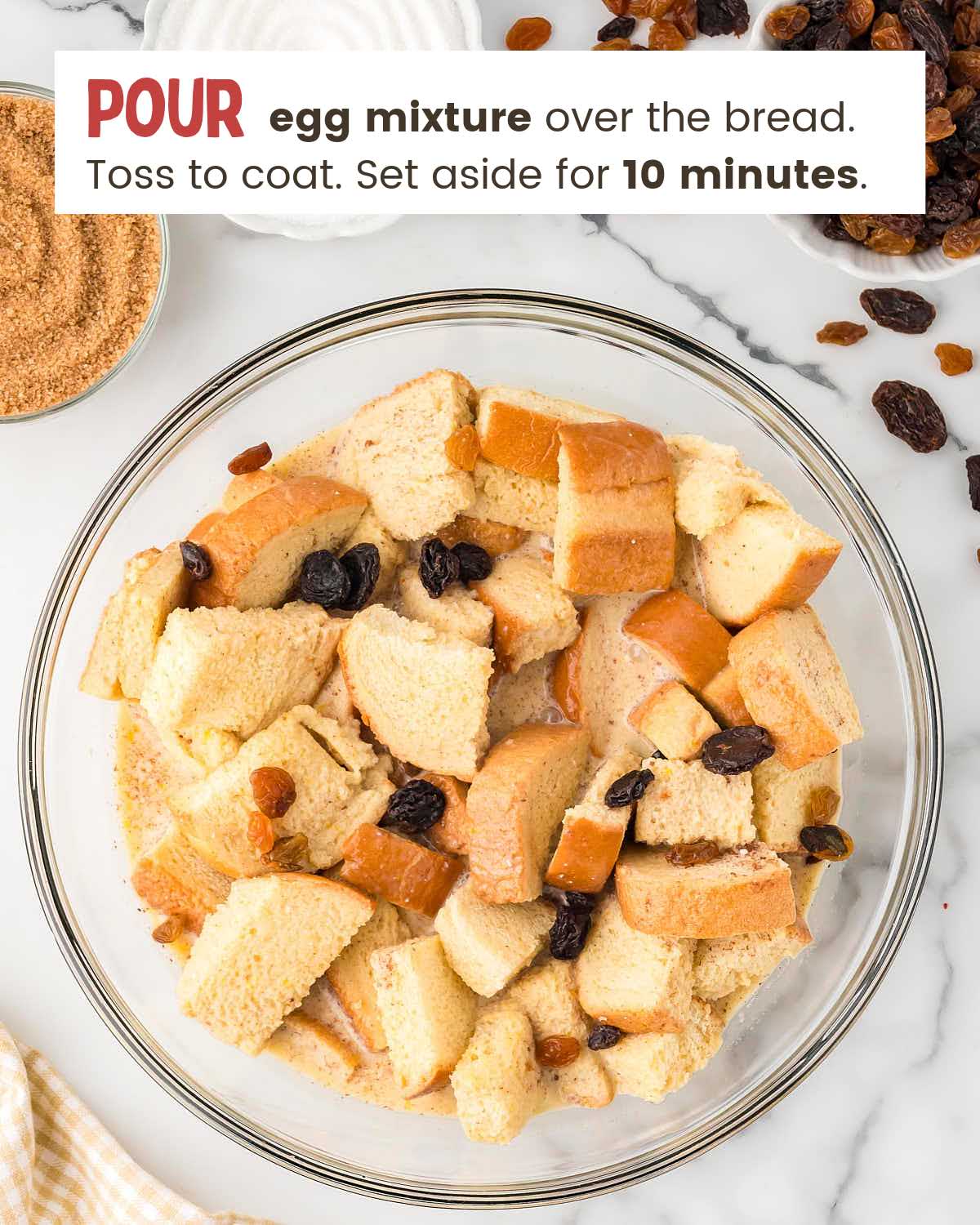 Bread cubes and raisins in a bowl with an egg mixture poured over them.