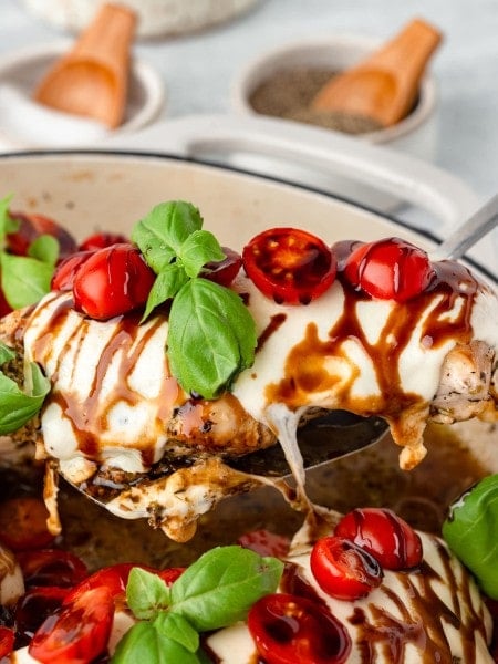 A serving spoon holding a slice of Chicken Caprese out of the skillet.