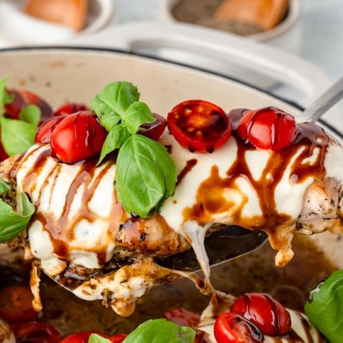 A serving spoon holding a slice of Chicken Caprese out of the skillet.