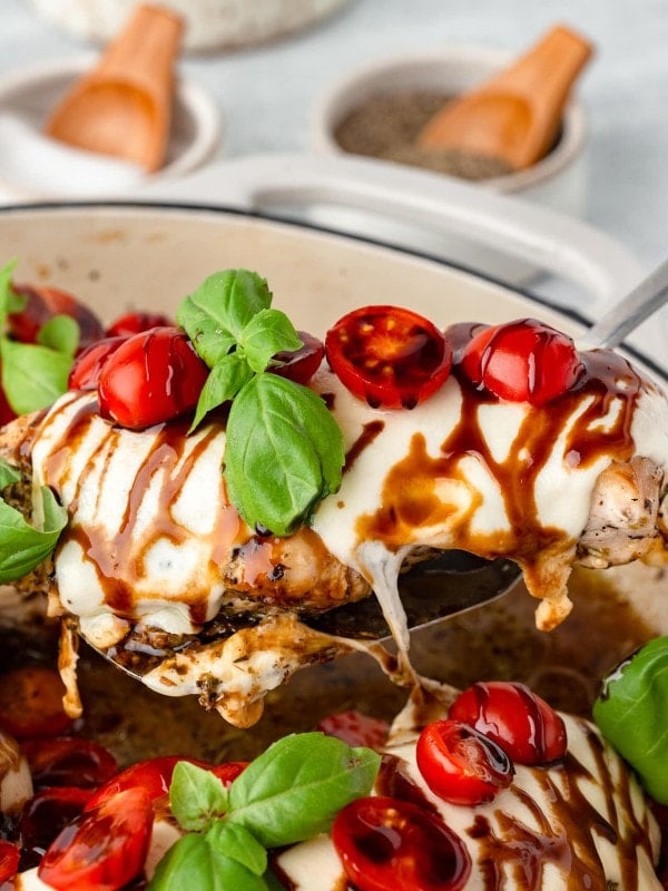 A serving spoon holding a slice of Chicken Caprese out of the skillet.