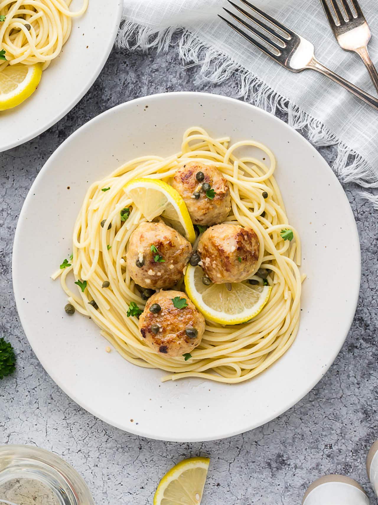 Chicken Piccata Meatballs served over spaghetti on a white plate.