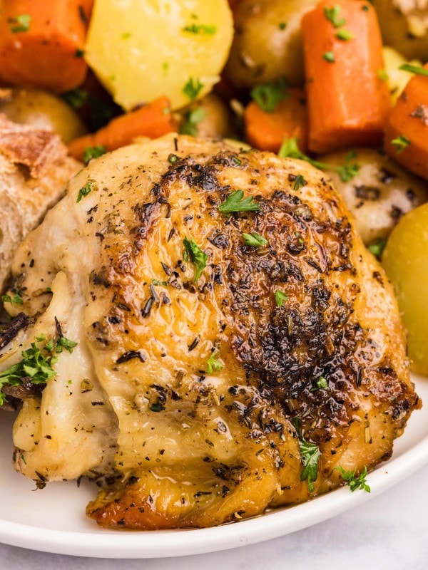 Closeup of a Slow Cooker chicken thigh on a white plate.
