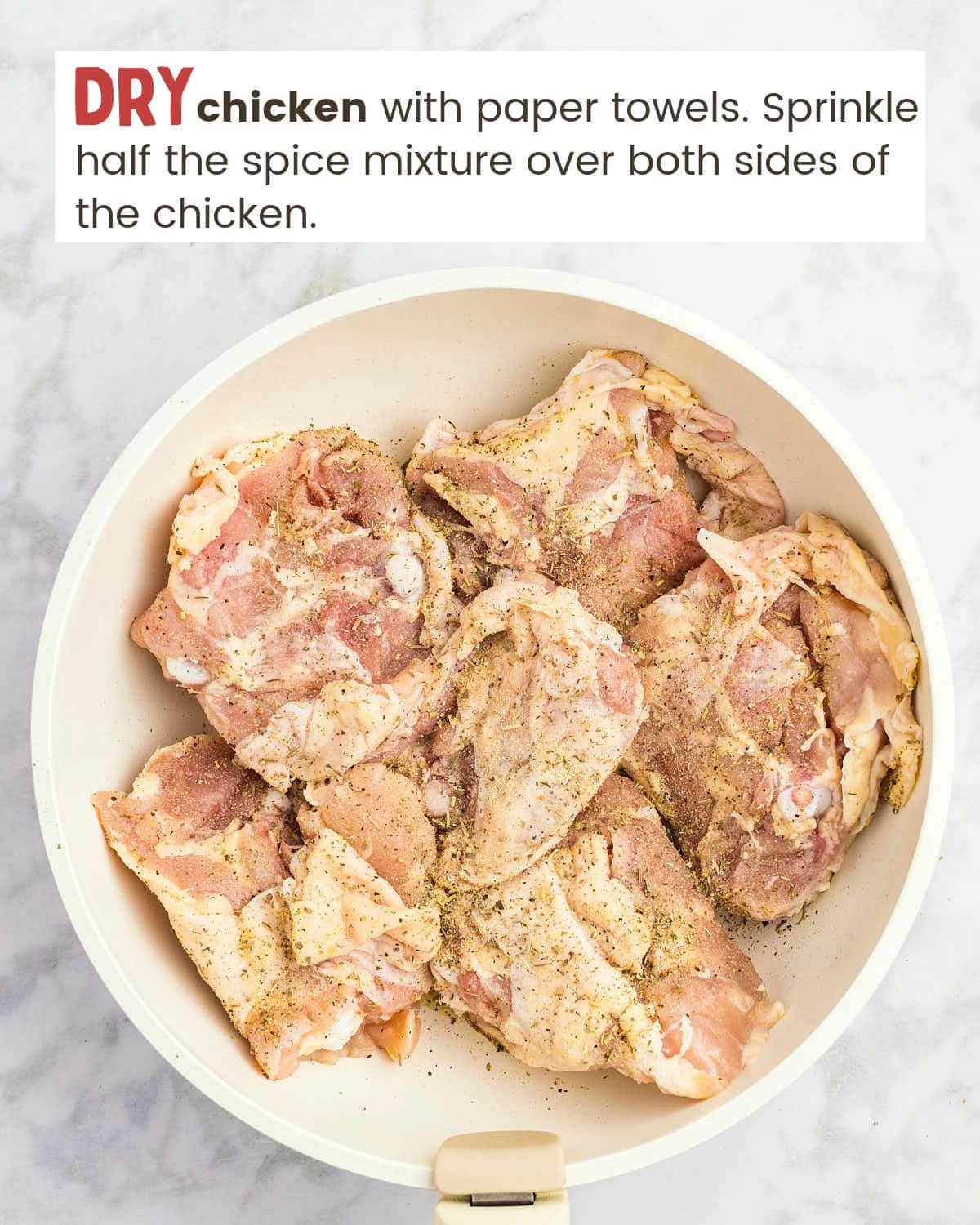 Chicken thighs in a skillet sprinkled with spice mix.