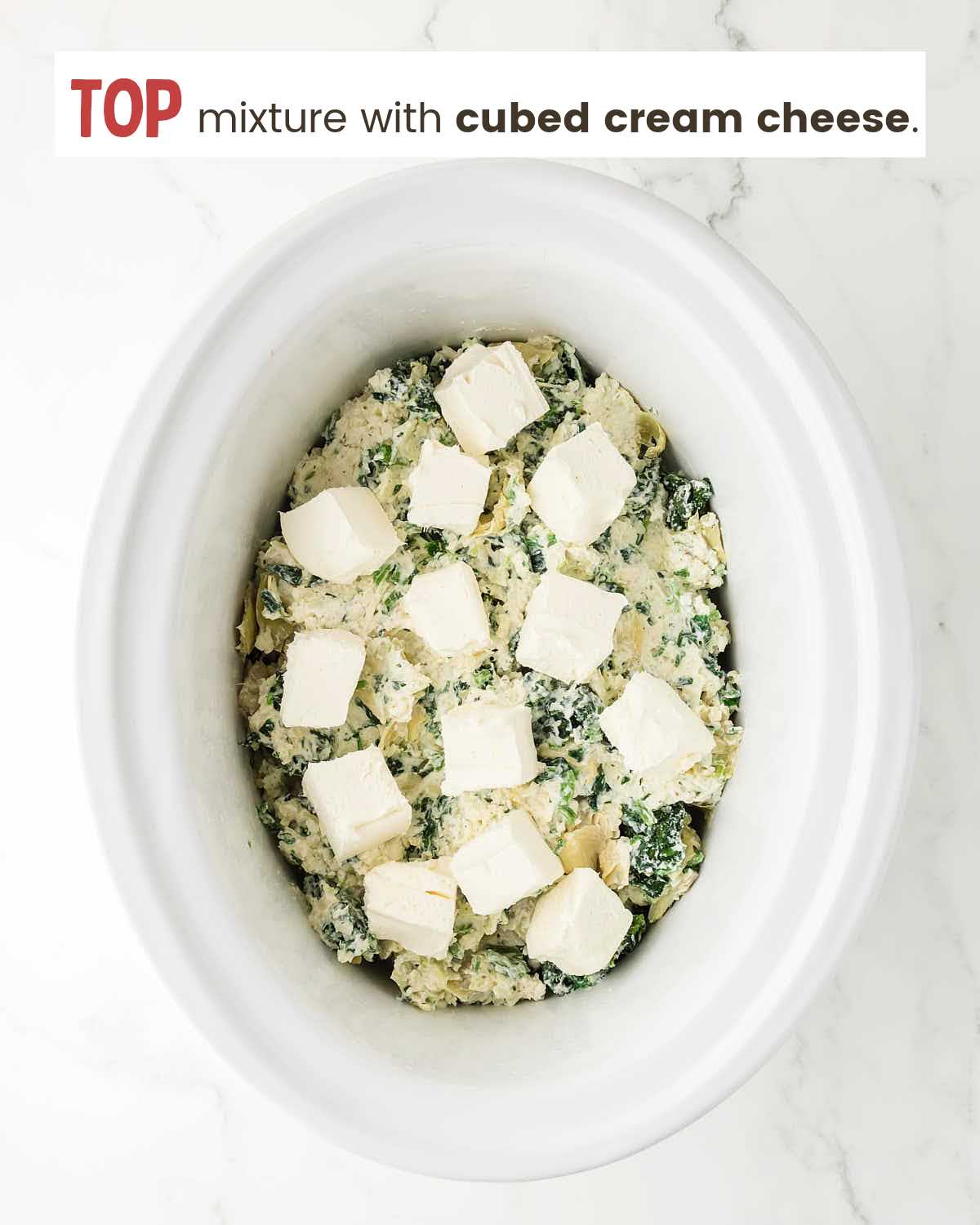 Spinach artichoke mixture in a slow cooker topped with cubed cream cheese.