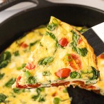 A hot slice of frittata being lifted from a cast iron skillet.