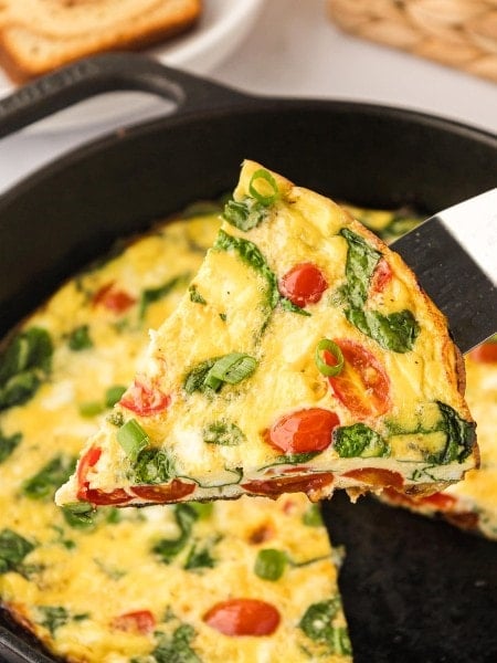 A hot slice of frittata being lifted from a cast iron skillet.