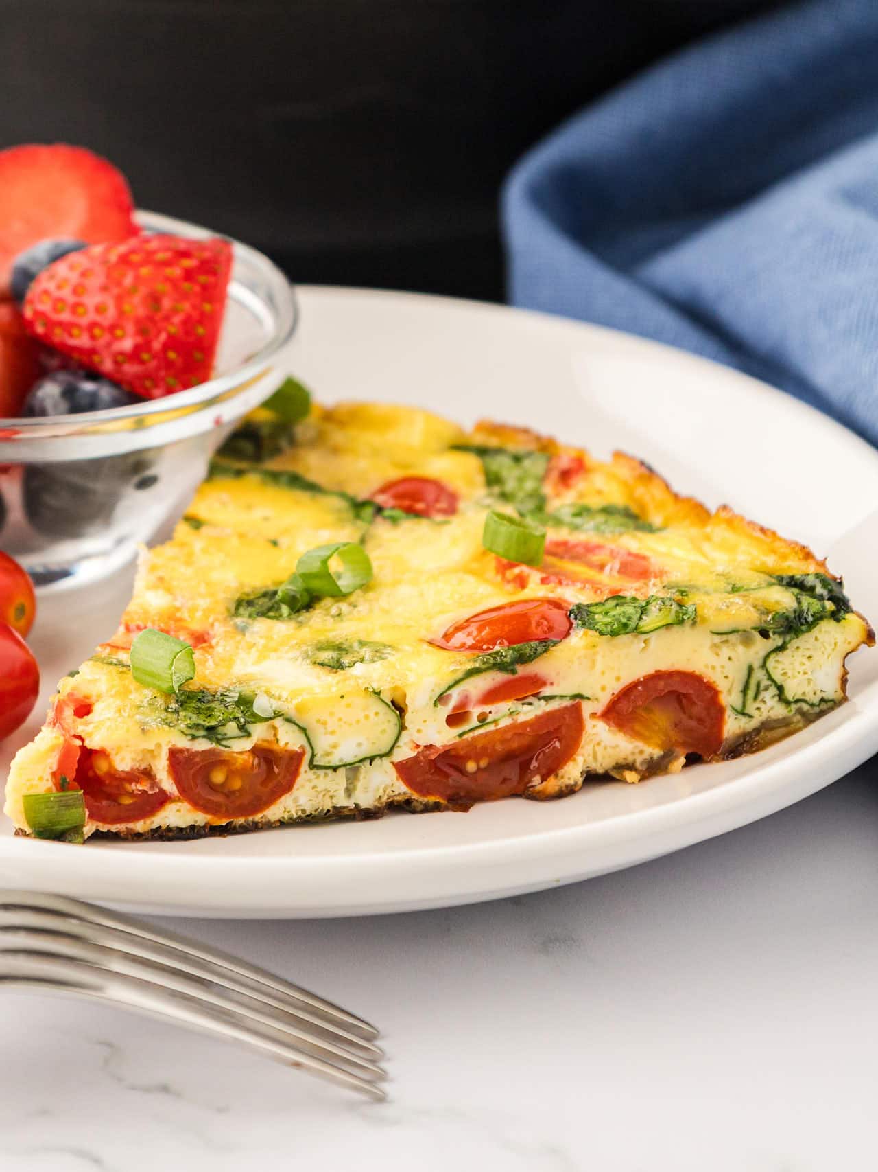 A slice of Frittata on a white plate with a side of fresh fruit.