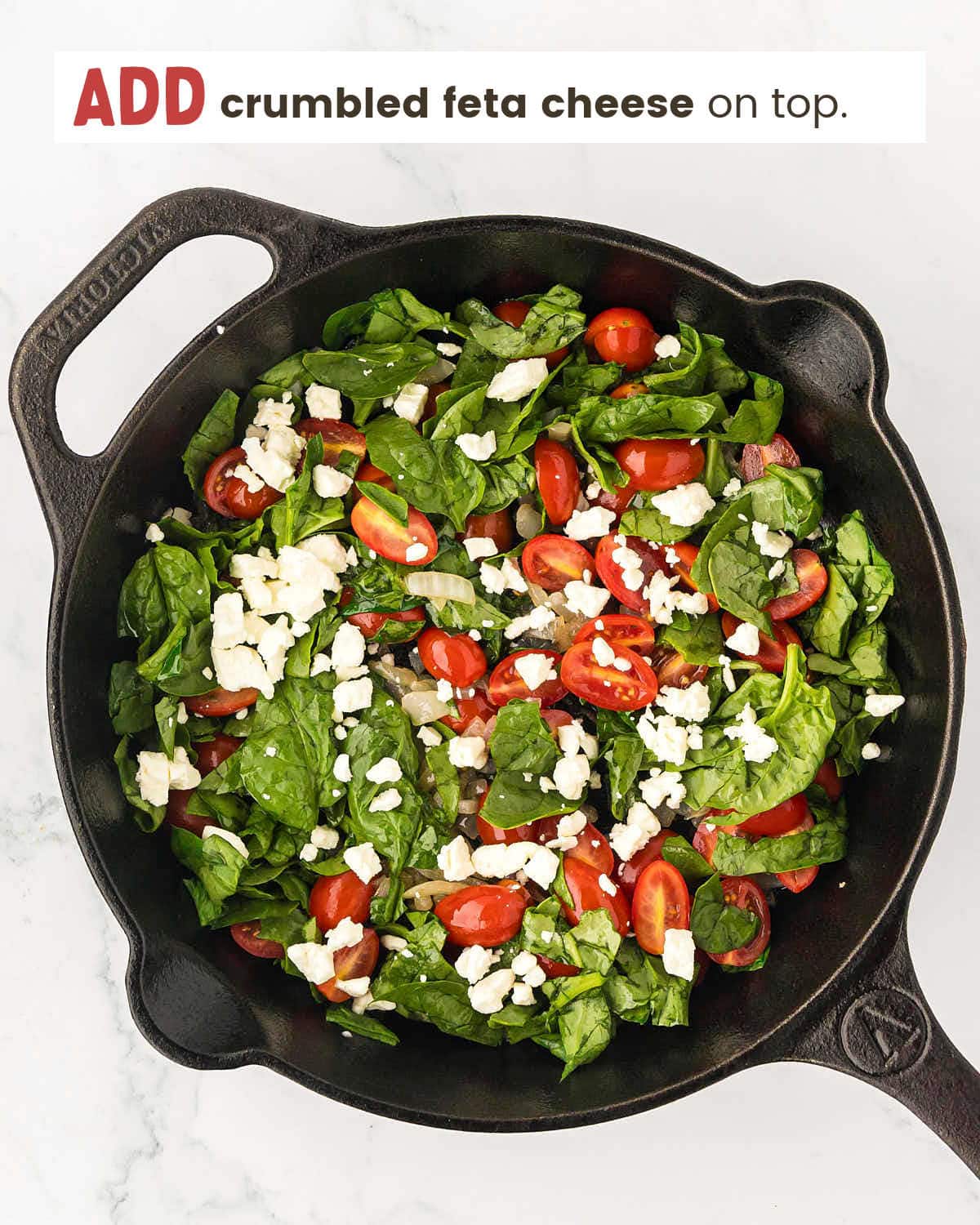 Feta cheese, spinach, and cherry tomatoes in a cast iron pan.