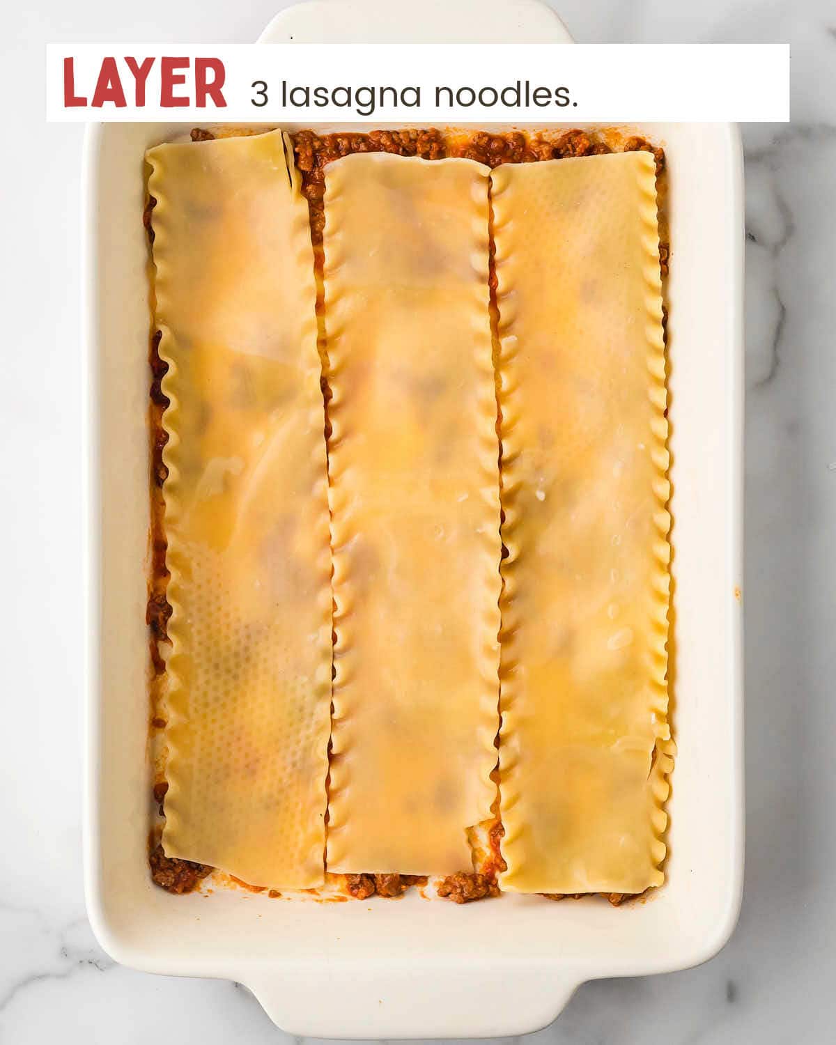 Meat sauce topped with lasagna noodles in baking dish.