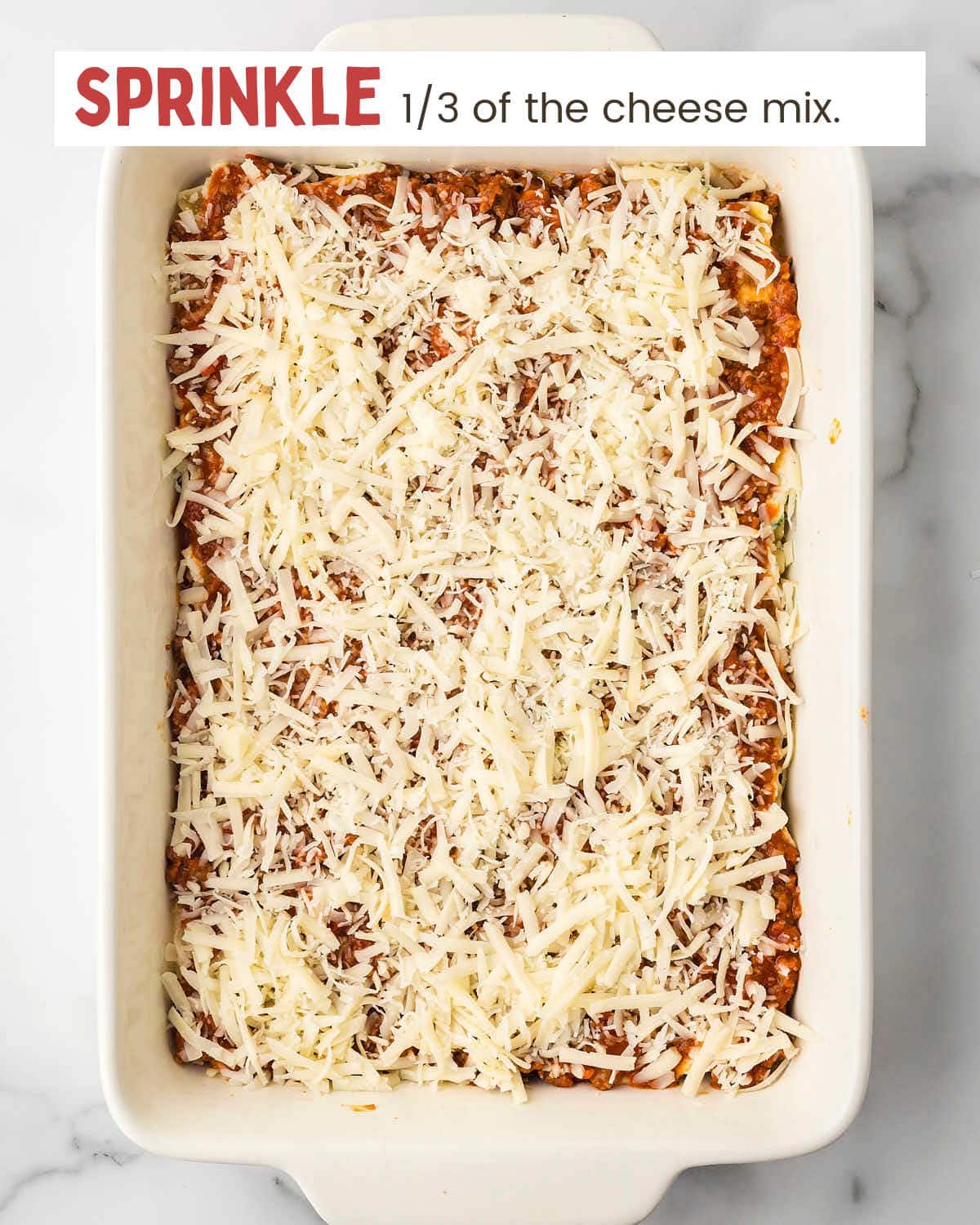 Cheeses sprinkled over meat sauce layer of lasagna in a baking dish.