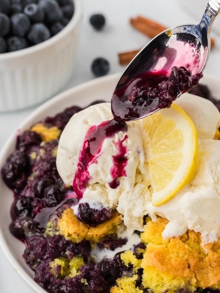 Pouring blueberry sauce over the Lemon Blueberry Dump Cake served with vanilla ice cream.