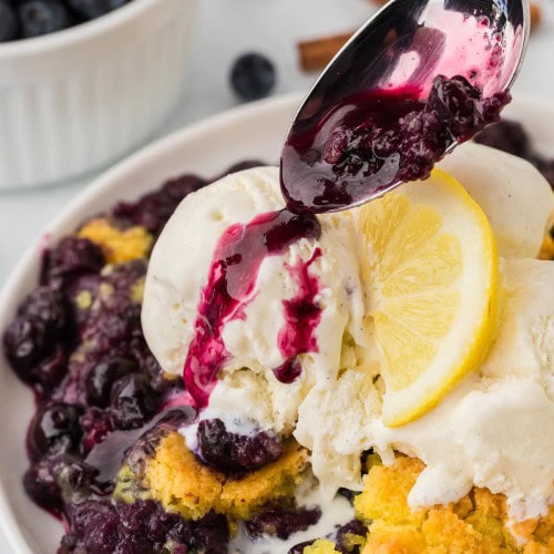 Pouring blueberry sauce over the Lemon Blueberry Dump Cake served with vanilla ice cream.