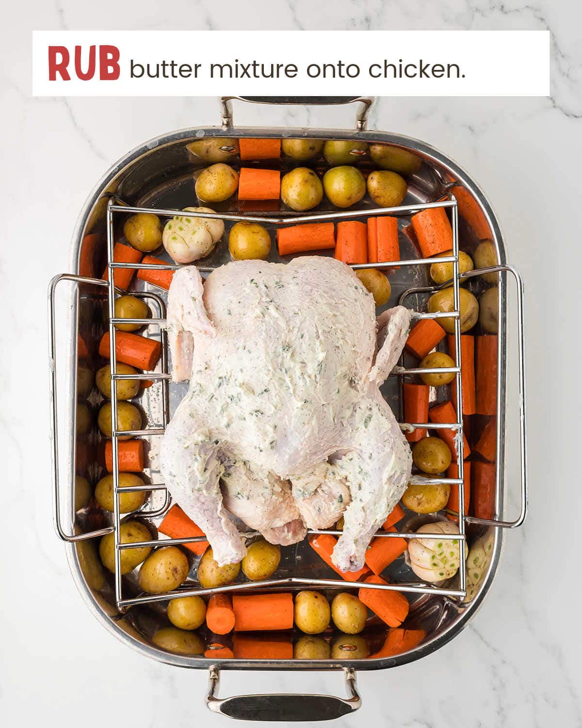 A butter mixture on a chicken on a roasting rack over potatoes and carrots.