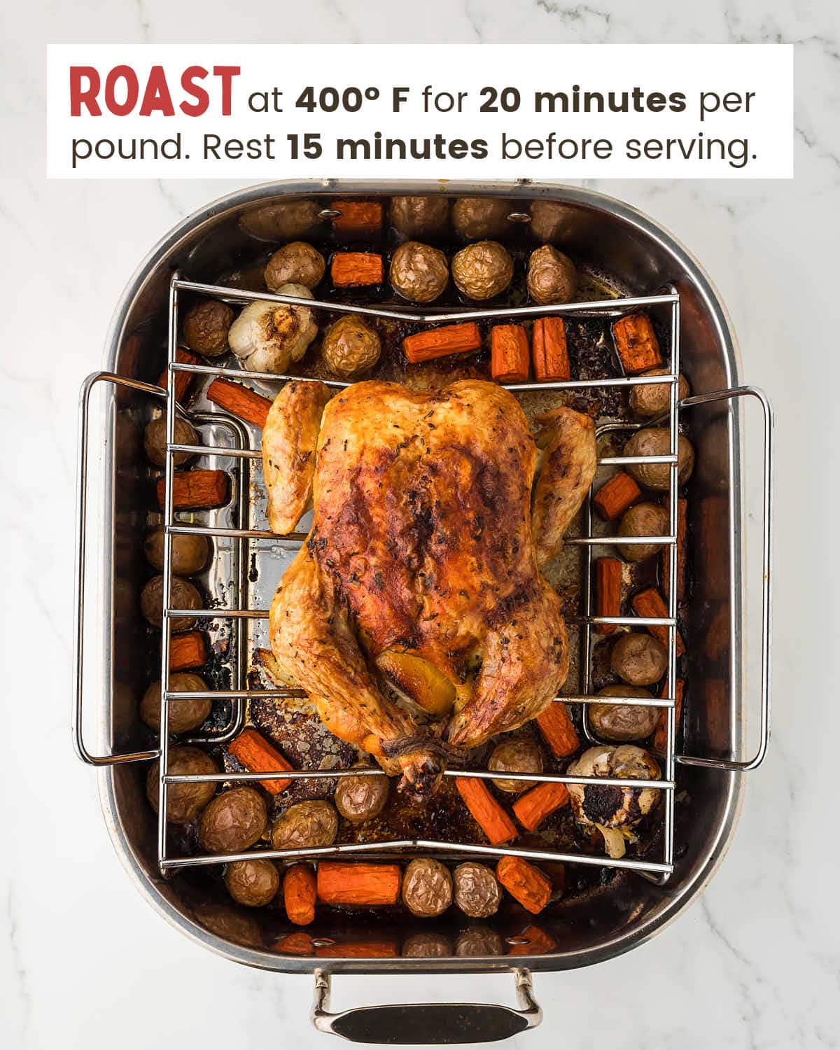Roasted chicken on a roasting rack over roasted carrots and potatoes in a roasting pan.