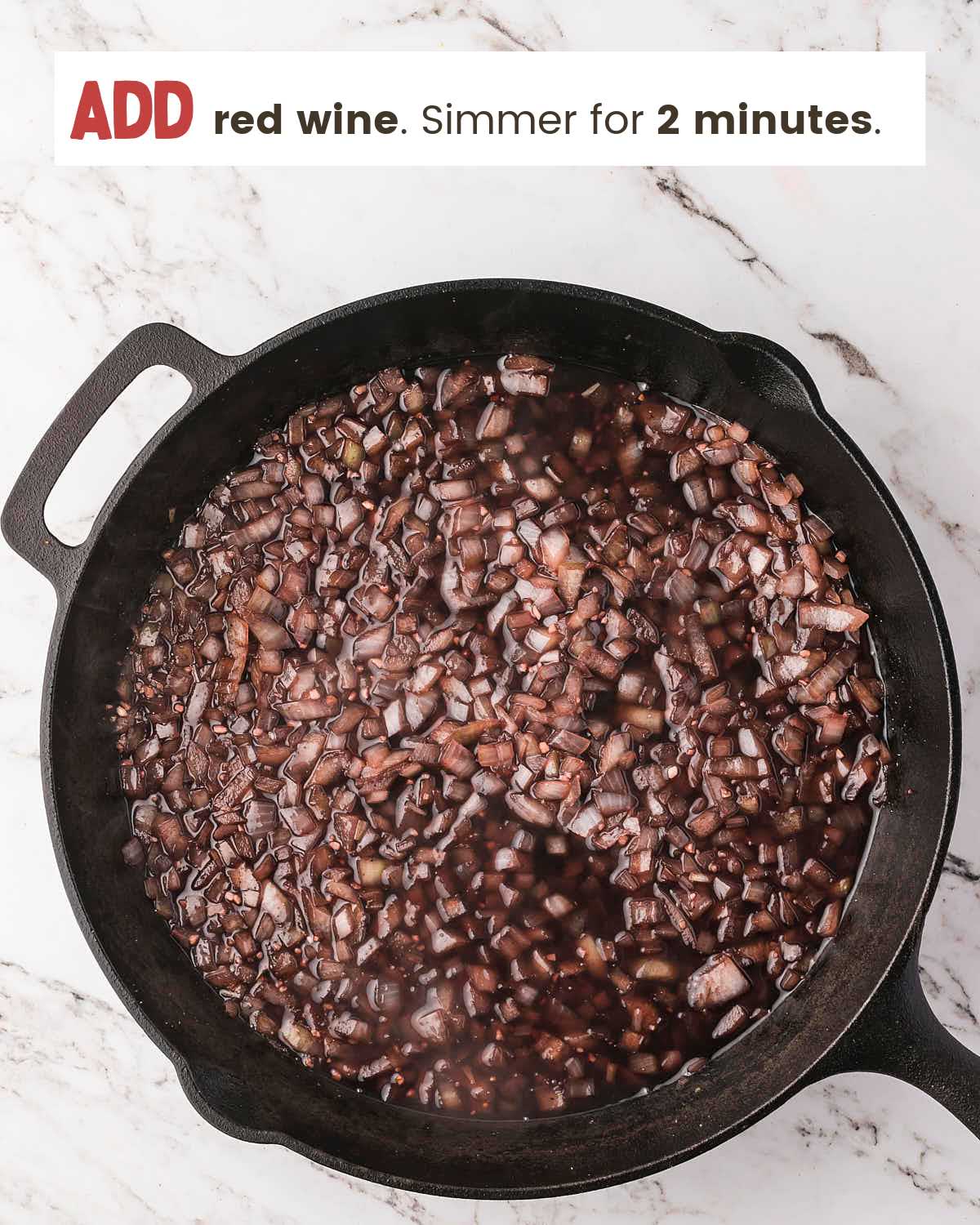 Red wine simmering with onions and garlic in a cast iron skillet.