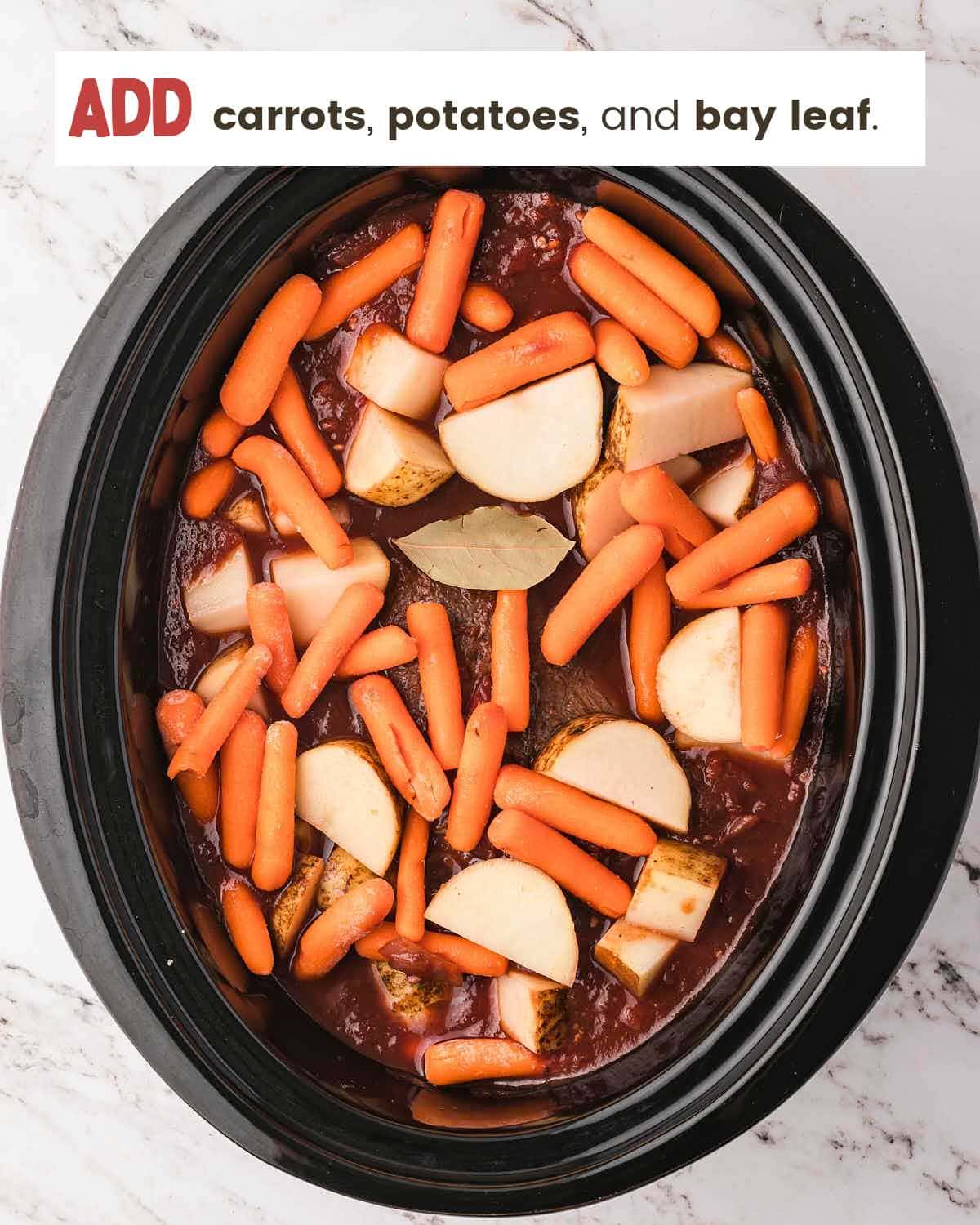 Baby carrots, potato chunks, and a bay leaf added to a slow cooker with tomato sauce.