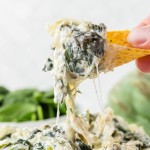 A tortilla chip filled with Slow Cooker Spinach Artichoke Dip.