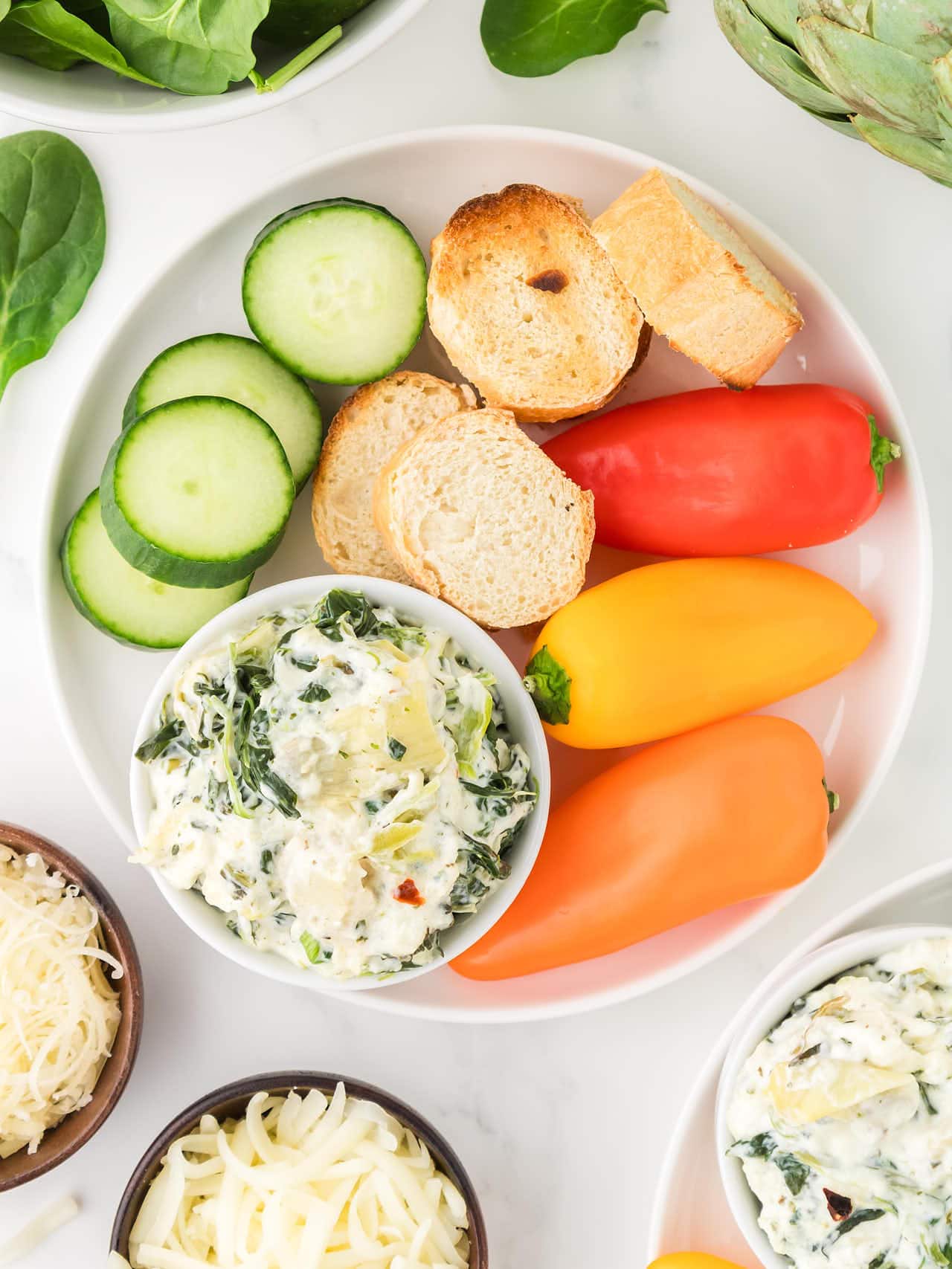 Top down view of veggies on a plate with a bowl of Slow Cooker Spinach Artichoke Dip.
