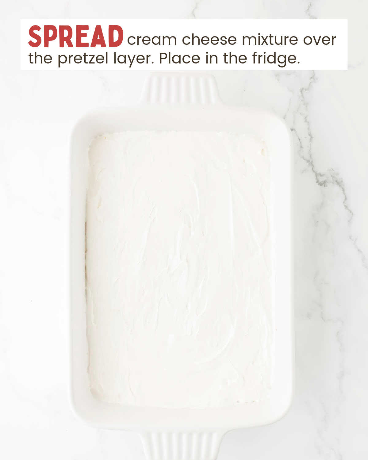 Cream cheese layer of a strawberry pretzel layer in a baking dish.