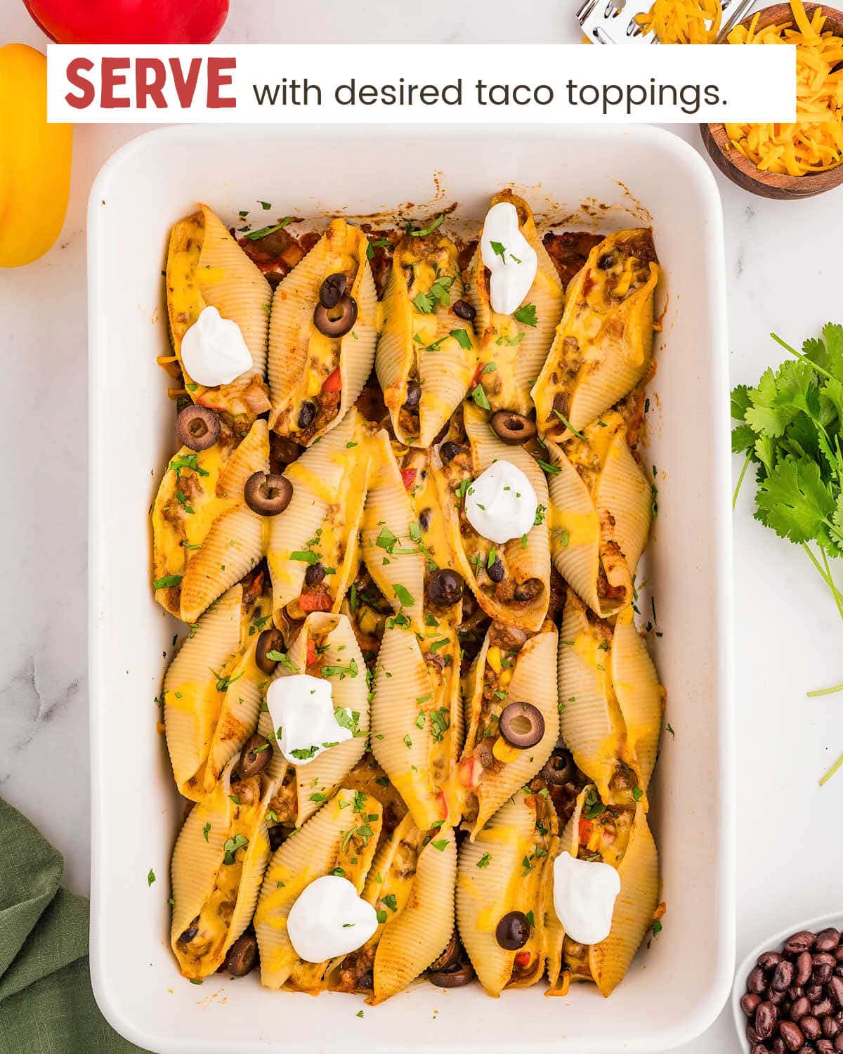 Stuffed pasta shells topped with cheese, sliced jalapeños, and sour cream in a baking dish.