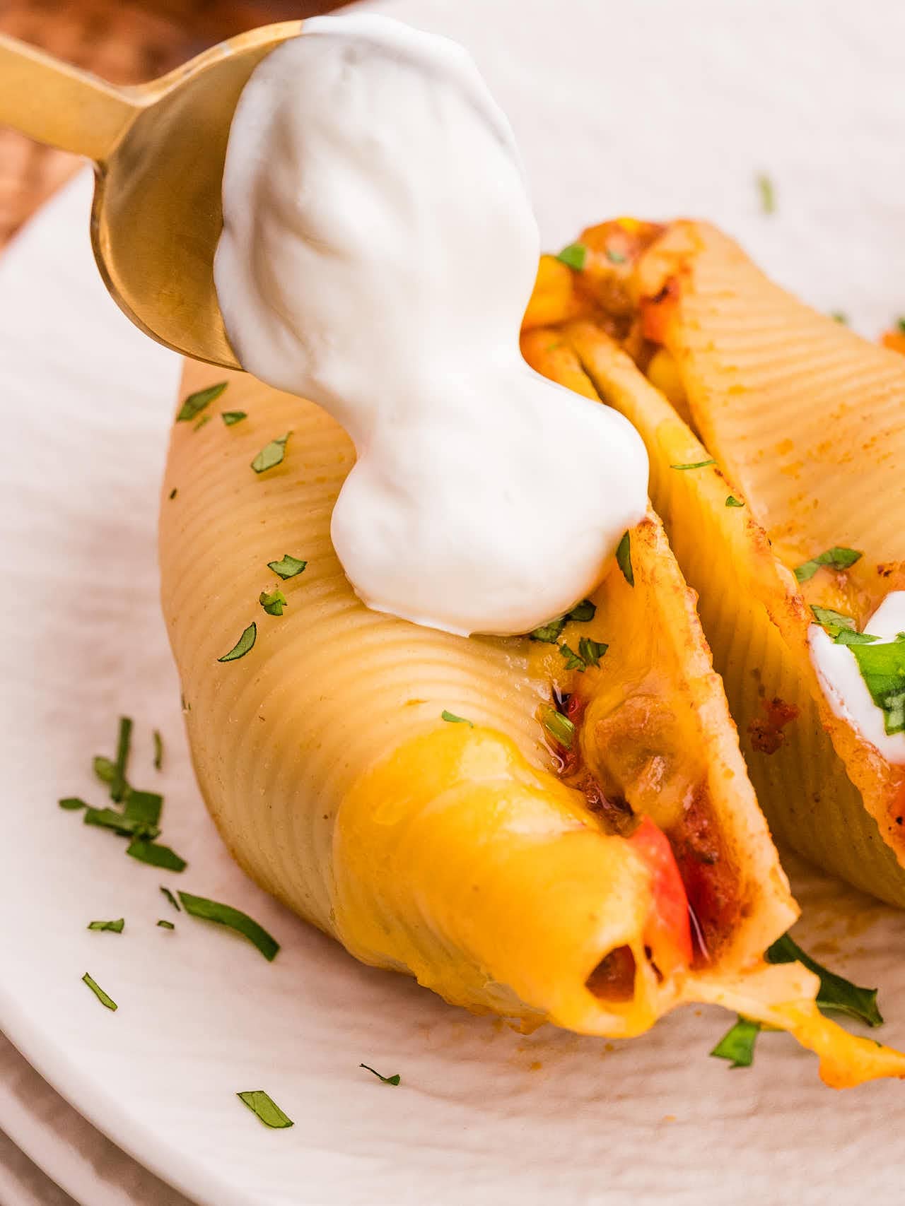 Dropping a spoonful of sour cream onto a cheesy Taco Stuffed Shells.